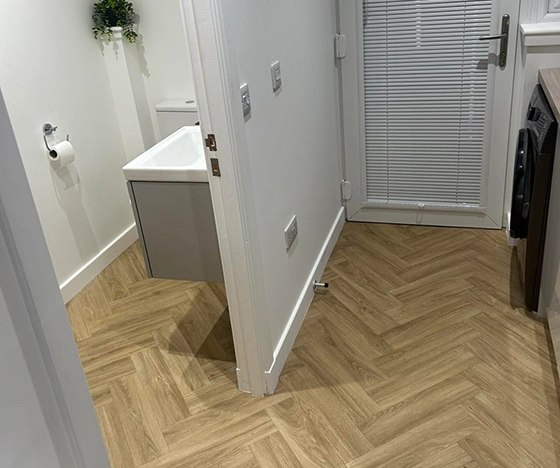 Premium light oak herringbone flooring and white venetian blinds installed by Ness Blinds & Floors in an Inverness home utility room and cloakroom.
